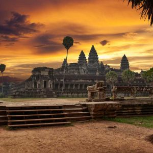 Ancient temple complex at sunset with palm trees and orange sky