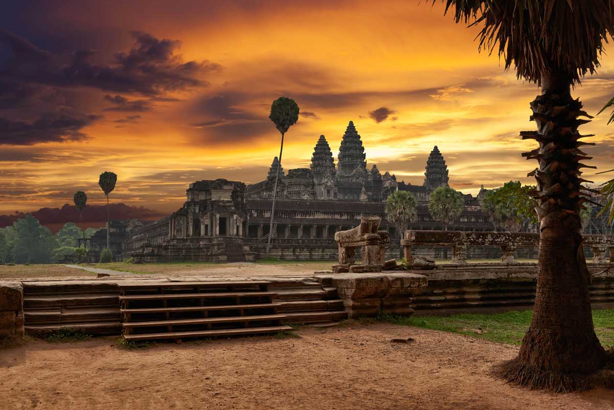 Ancient temple complex at sunset with palm trees and orange sky