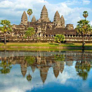 Angkor Wat temple reflected in water with palm trees and blue sky