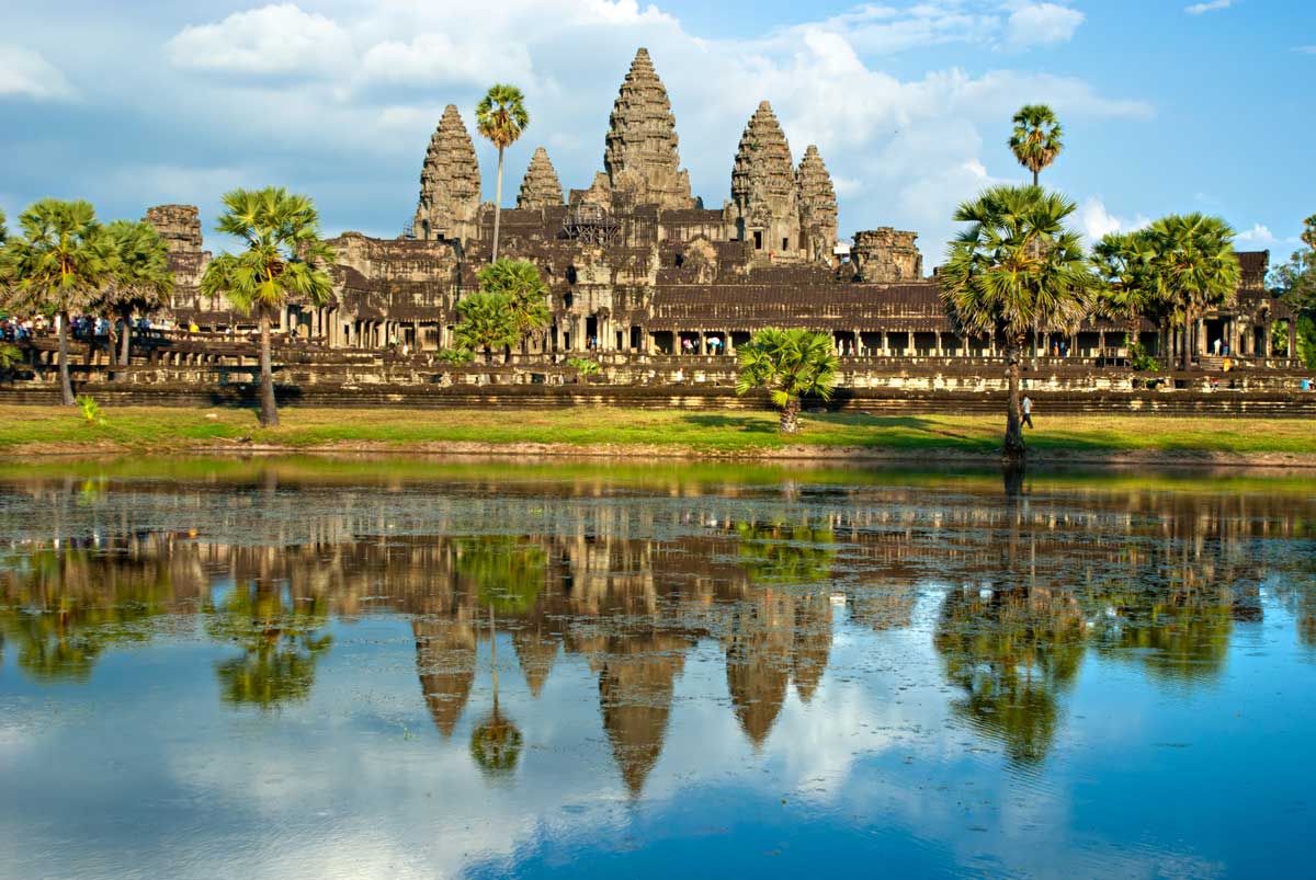 Angkor Wat temple reflected in water with palm trees and blue sky