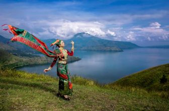 Woman in traditional Indonesian dress on hill with lake and mountains