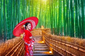 Woman in red kimono with umbrella stands on bamboo forest path