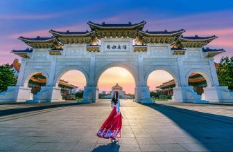 Woman in traditional clothing walking towards large white archway at sunrise