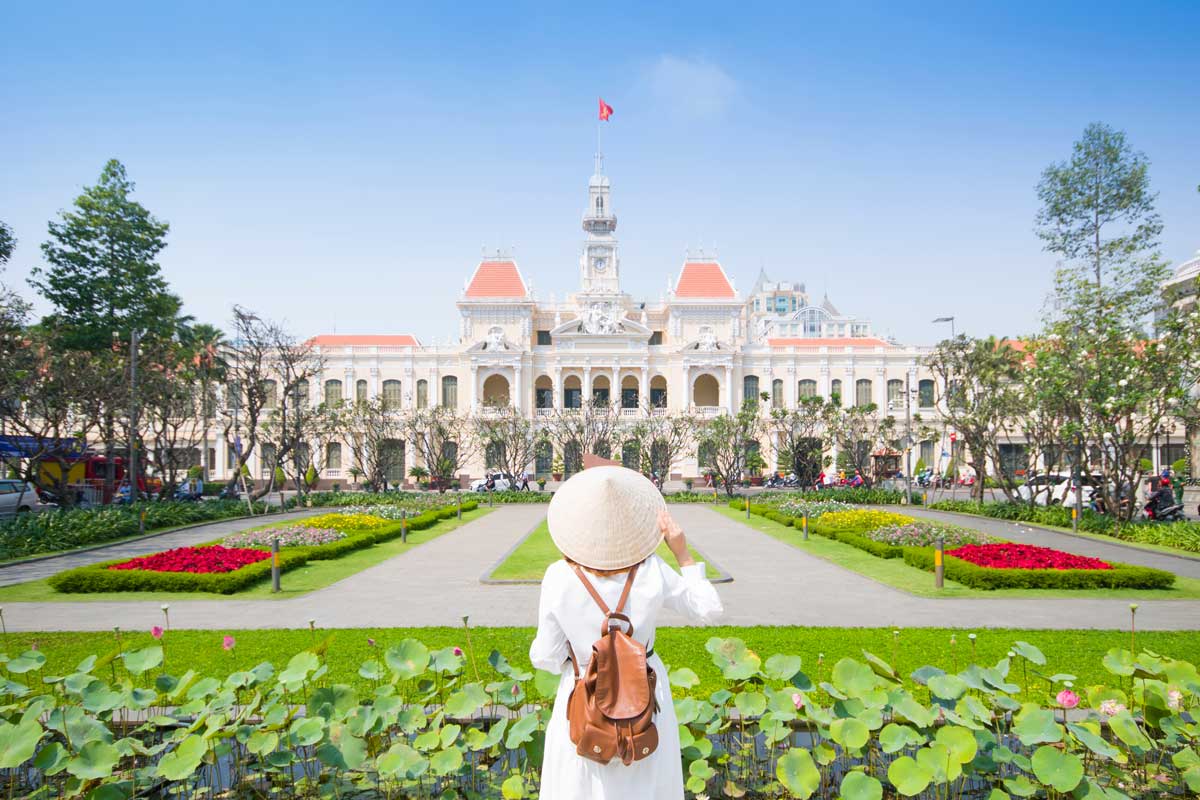 Woman in conical hat facing colonial city hall building with gardens and lotus pond