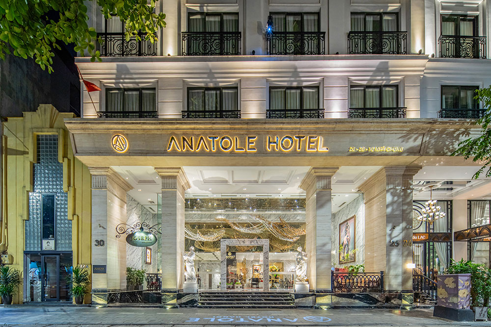 Entrance of Anatole Hotel Hanoi illuminated at night with classical columns and statues