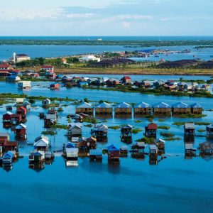 Aerial view of colorful stilt houses built over flooded land surrounded by water and vegetation.