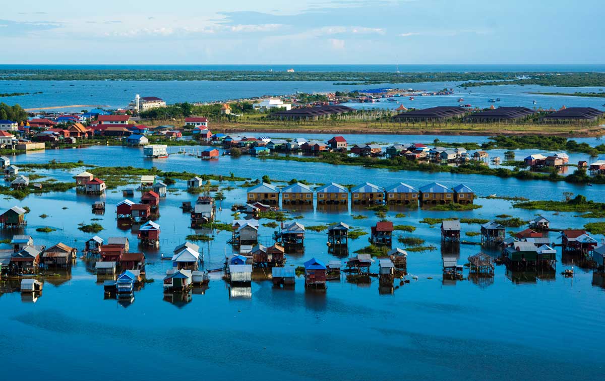 Aerial view of colorful stilt houses built over flooded land surrounded by water and vegetation.