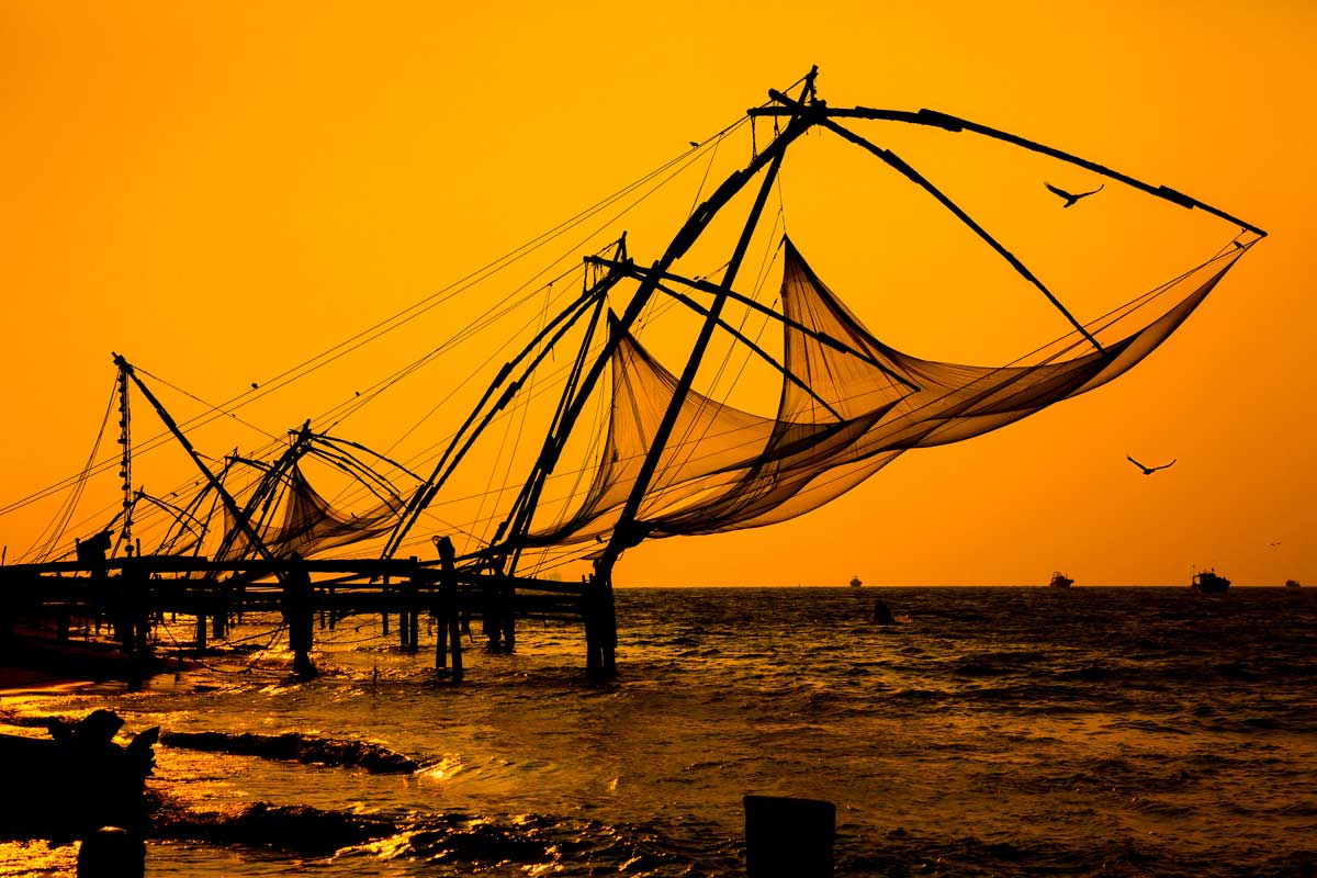 Chinese fishing nets silhouetted at sunset over the sea with flying birds