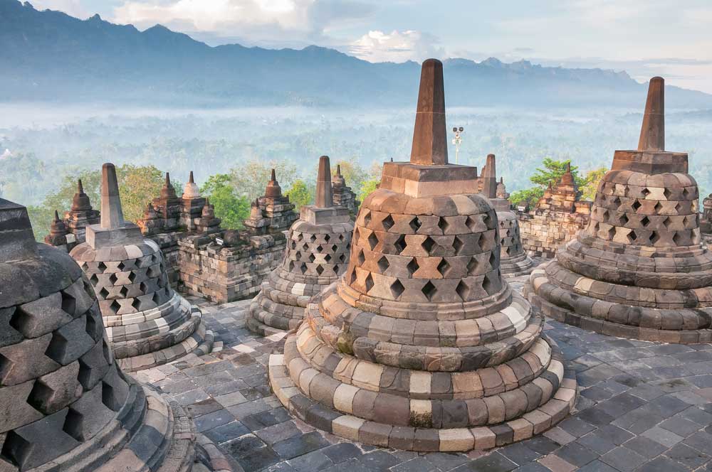 Ancient stone stupas on temple terrace with misty mountains behind