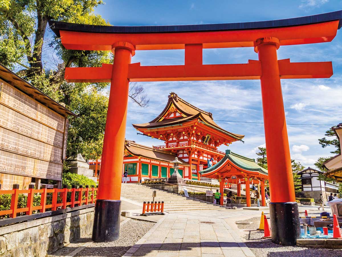 Red torii gate at entrance to traditional Japanese shrine with visitors