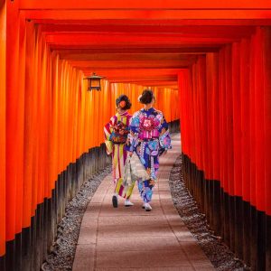 Two women in colorful kimonos walking through a tunnel of red torii gates