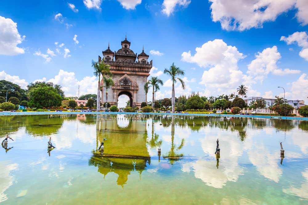 Patuxai monument reflected in pond with palm trees and blue sky