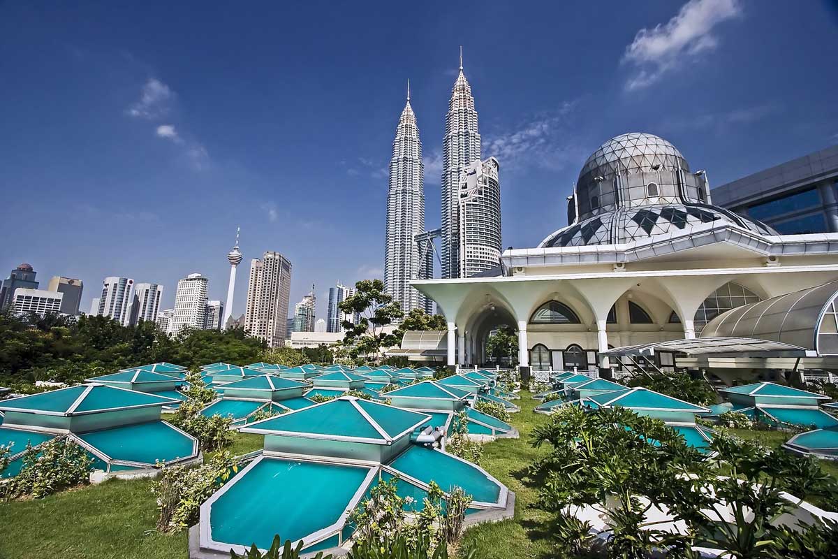 Petronas Twin Towers and city skyline with garden and dome in foreground under blue sky