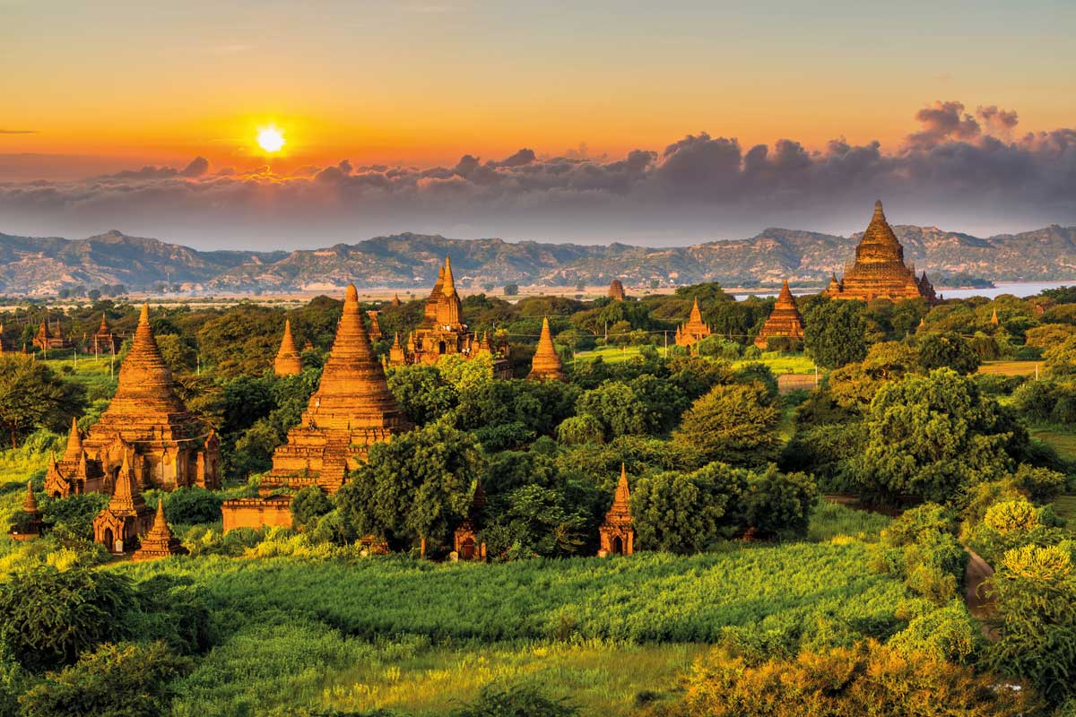 Sunset over ancient pagodas and green landscape with mountains and clouds in background