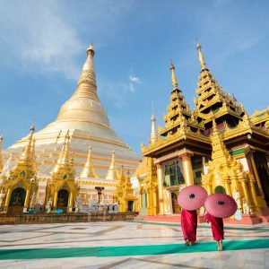 Two monks with umbrellas walking near golden Buddhist temple and pagoda