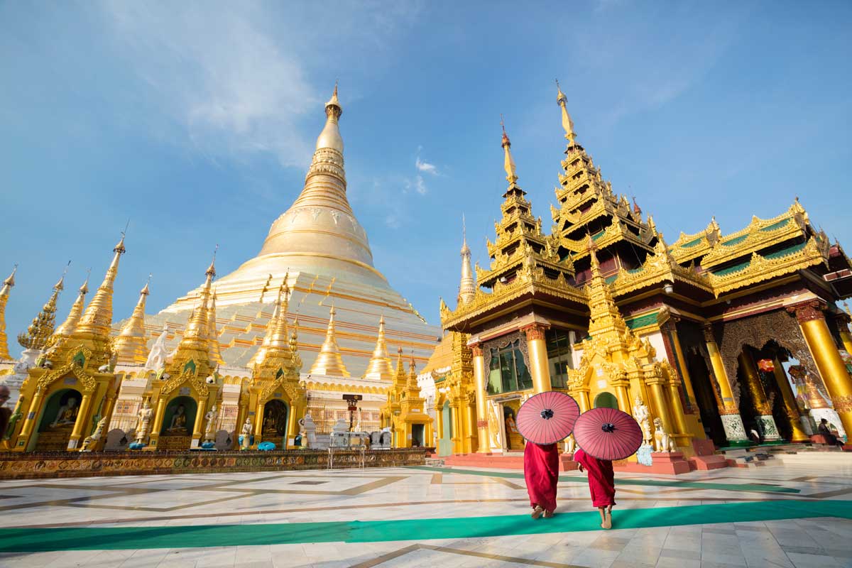 Two monks with umbrellas walking near golden Buddhist temple and pagoda