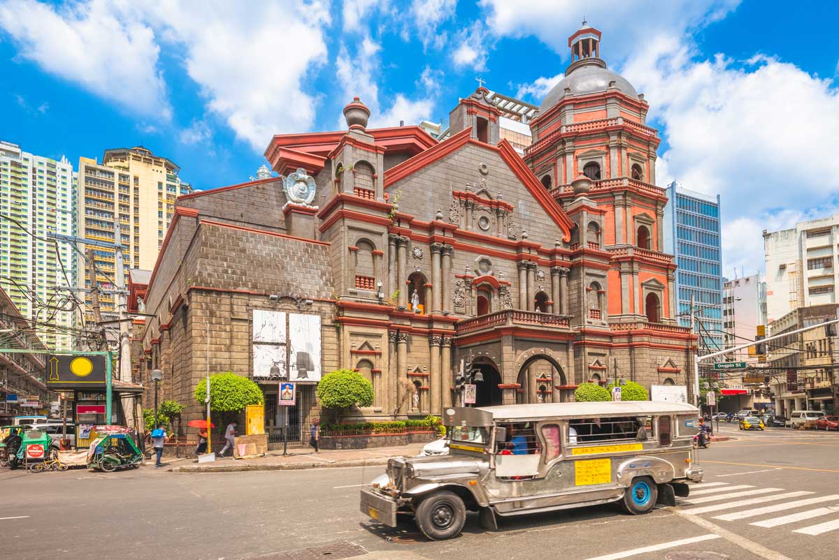 Historic stone church with silver jeepney on city street under blue sky