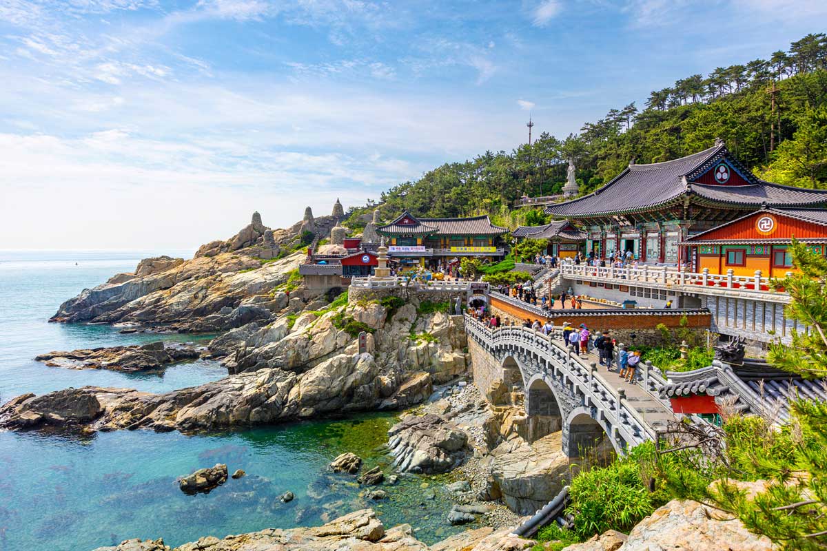 Traditional Korean Buddhist temple complex on rocky coast with ocean and visitors