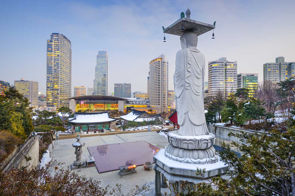 White Buddha statue overlooking temple courtyard with city skyline and evening light