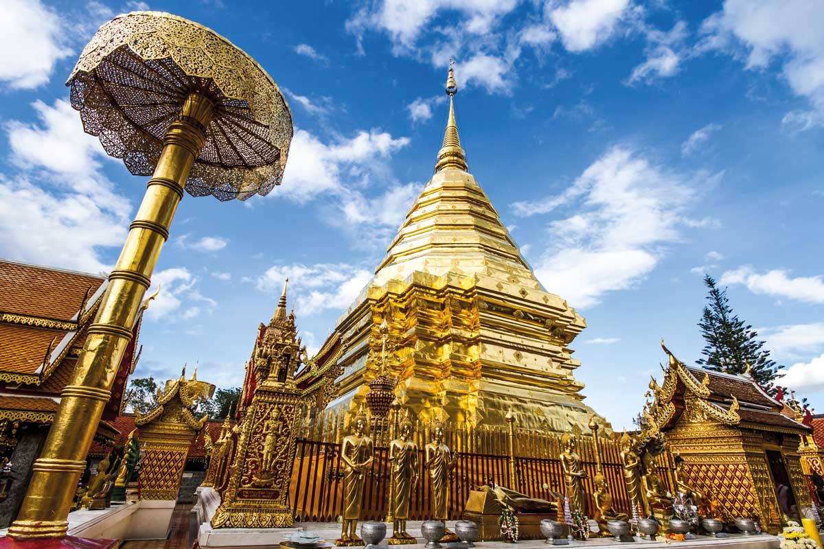 Golden Buddhist temple stupa and ornate statues under blue sky