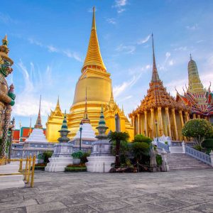 Golden Thai temple with spires and guardian statue against blue sky
