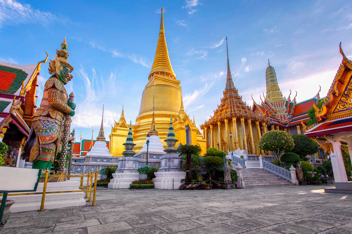 Golden Thai temple with spires and guardian statue against blue sky