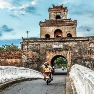 Motorcycles passing through ancient stone city gate over bridge