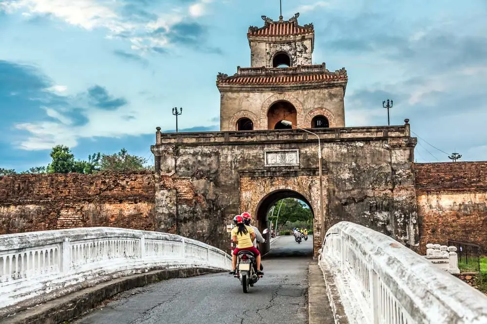 Motorcycles passing through ancient stone city gate over bridge