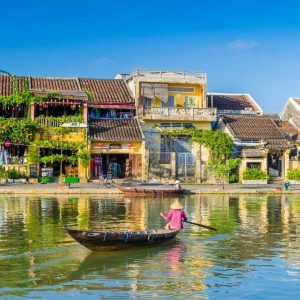 Person paddling wooden boat on river with colorful riverside buildings