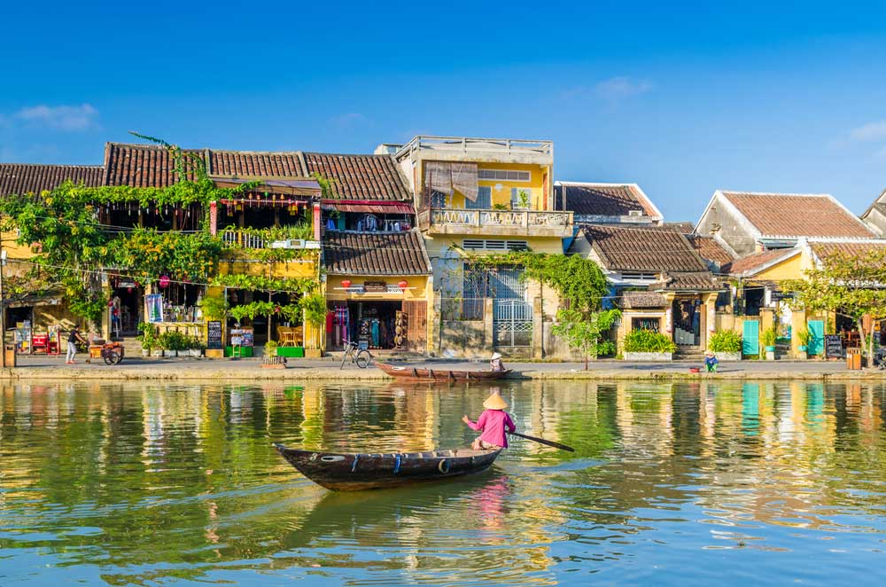 Person paddling wooden boat on river with colorful riverside buildings