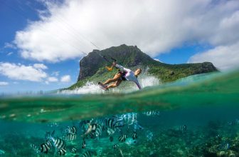 Woman kiteboarding on clear tropical water with coral reef and fish underwater