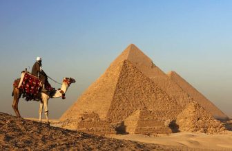 Camel rider overlooking the Great Pyramids of Giza at sunset in the desert