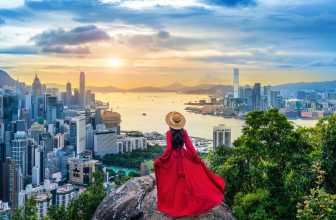 Woman in red dress overlooking Hong Kong skyline and harbor at sunset