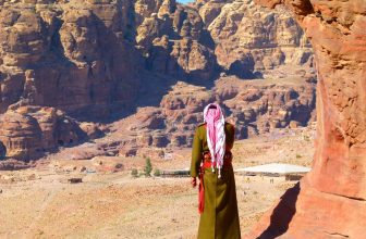 Man in traditional Jordanian clothing looking at rocky desert landscape.