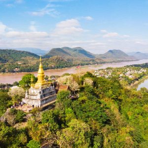 Golden stupa temple on green hill overlooking river and mountains under blue sky