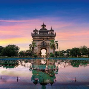 Patuxai monument reflected in pool at sunset with colorful skies
