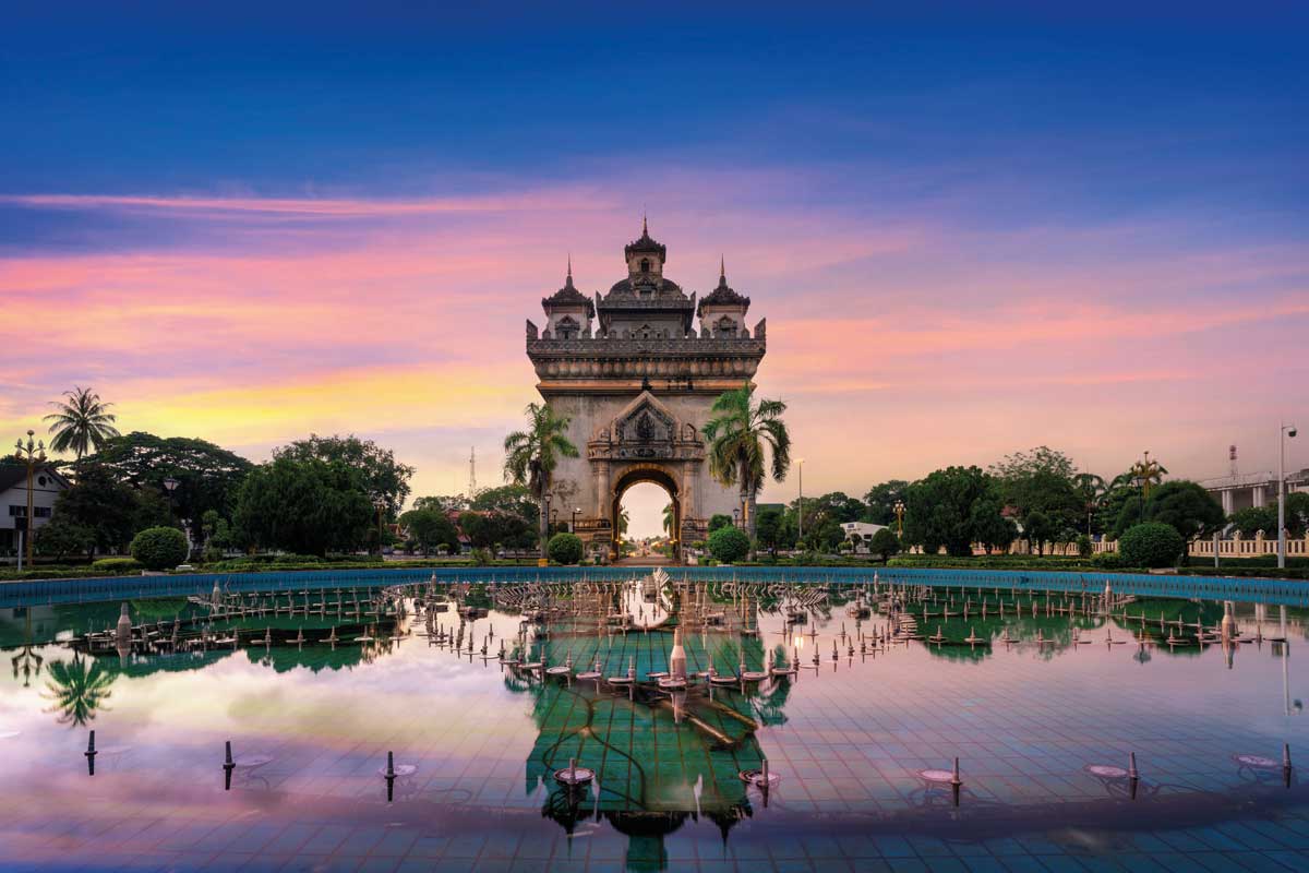 Patuxai monument reflected in pool at sunset with colorful skies