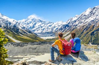 Couple seated on rock overlooking snowy mountains and valley in New Zealand
