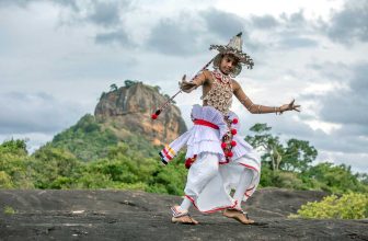 Traditional Sri Lankan Kandyan dancer performing with Lion Rock behind