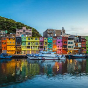 Colorful buildings by harbor with boats and green hillside in background under clear sky
