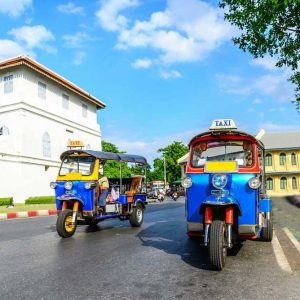 Two colorful tuk-tuk taxis on city street near white wall and buildings