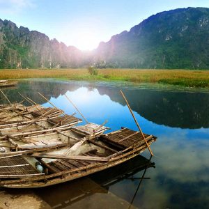 Bamboo boats docked on calm river with limestone mountains and sunrise