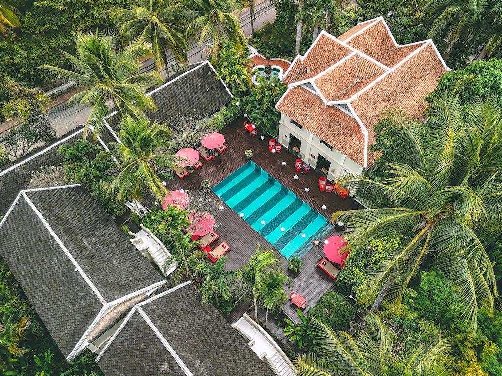 Aerial view of Villa Maly resort pool with red loungers surrounded by tropical plants in Laos