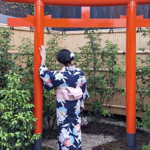 Woman in floral kimono touching red torii gate in garden