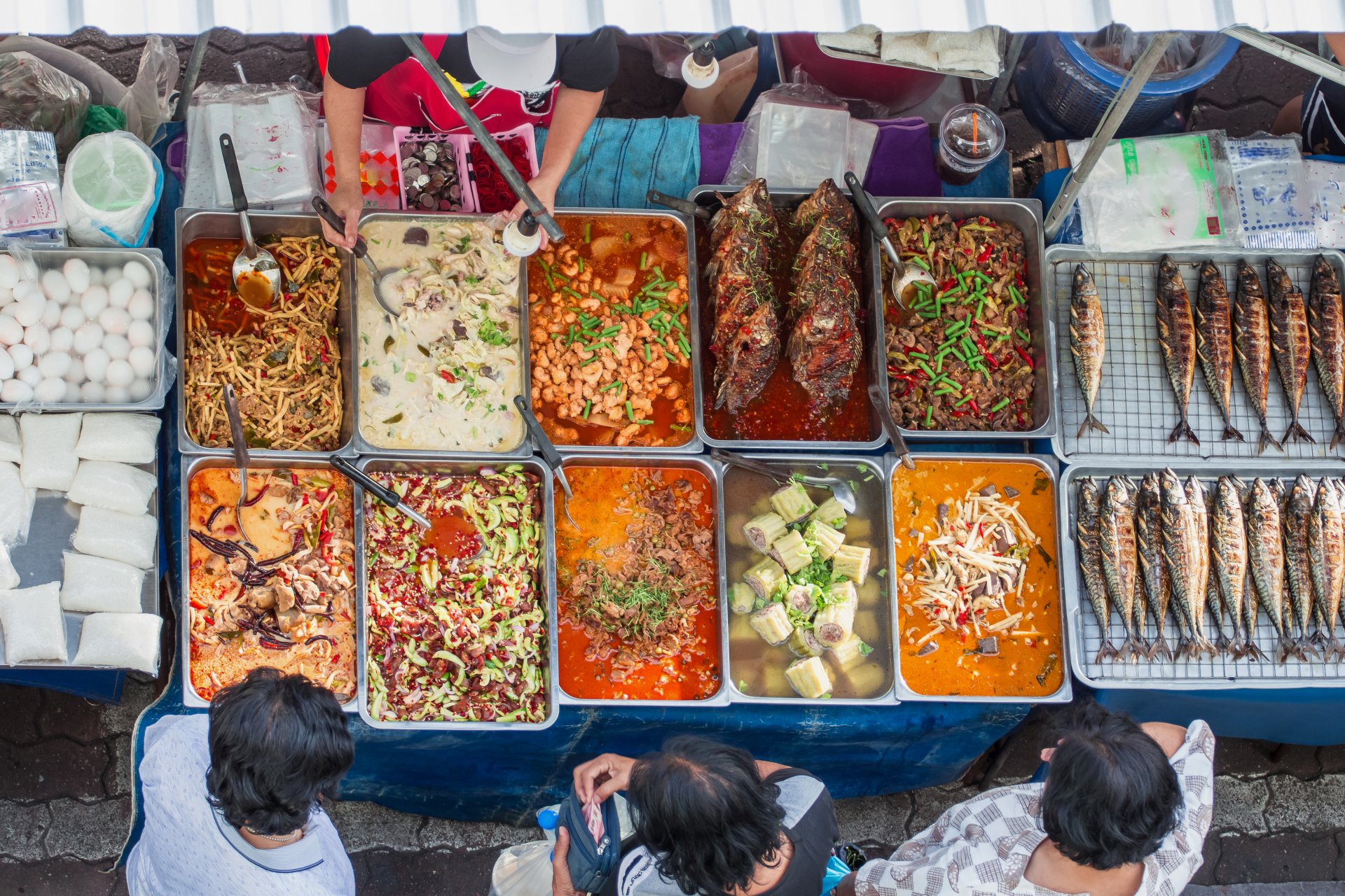 Top view of street food stall with trays of dishes and grilled fish