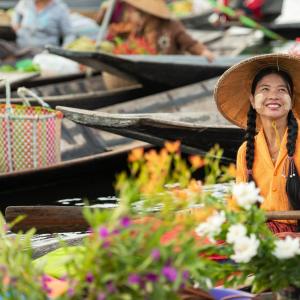 Smiling woman in traditional hat paddling a flower-filled wooden boat
