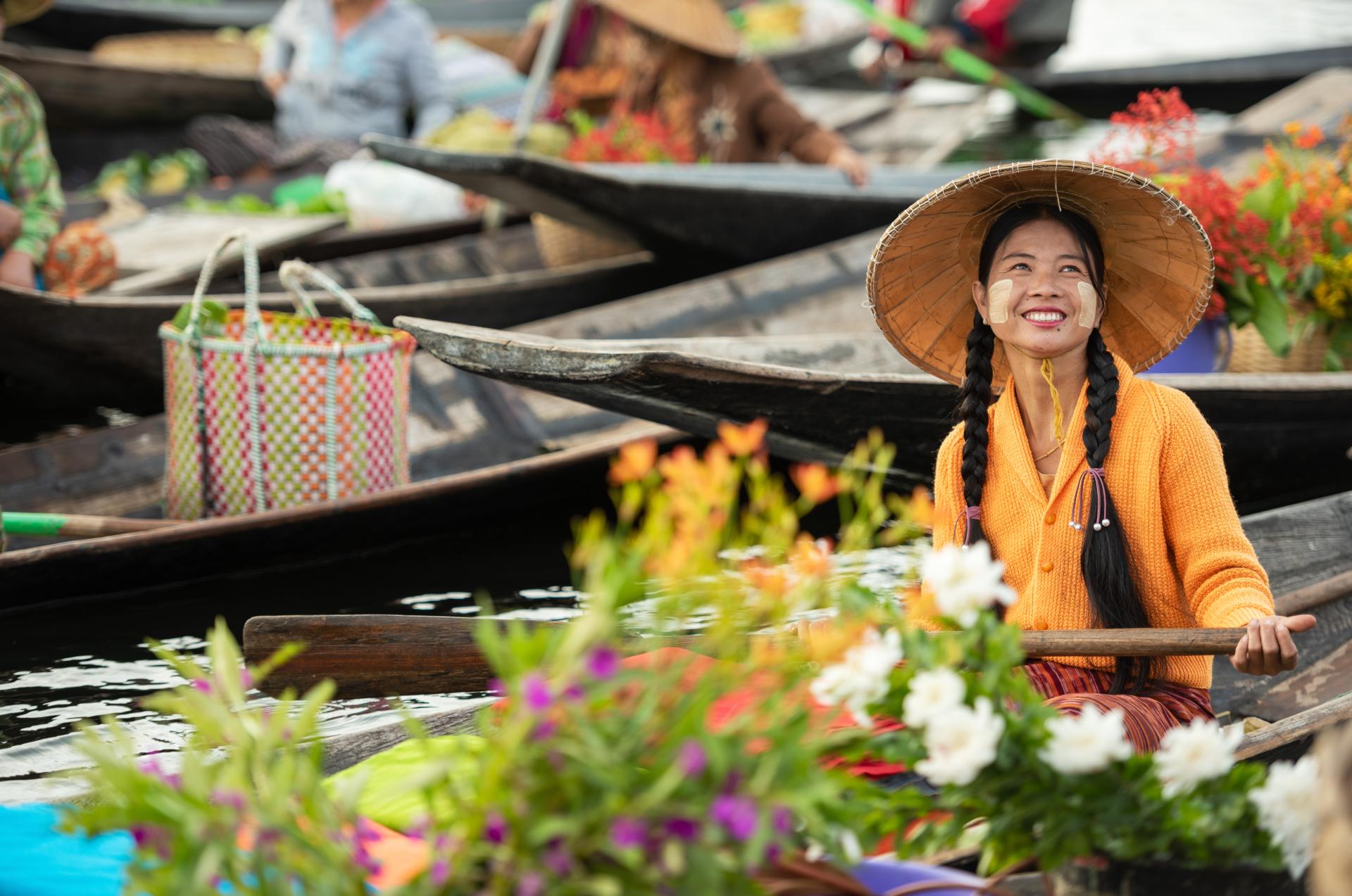 Smiling woman in traditional hat paddling a flower-filled wooden boat