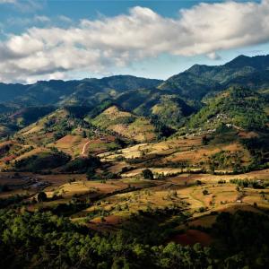 Scenic mountain valley with patchwork fields and scattered houses beneath cloudy blue sky