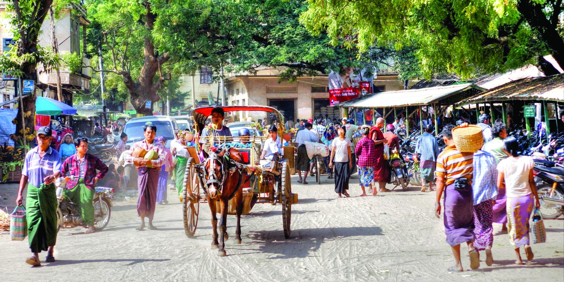 Crowded street with horse-drawn carriage and people walking under green trees