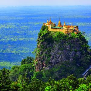 Golden Buddhist temple complex on top of a lush green rocky hill with distant plains